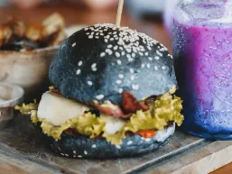 A charcoal-bun burger and a bright berry smoothie on a serving board