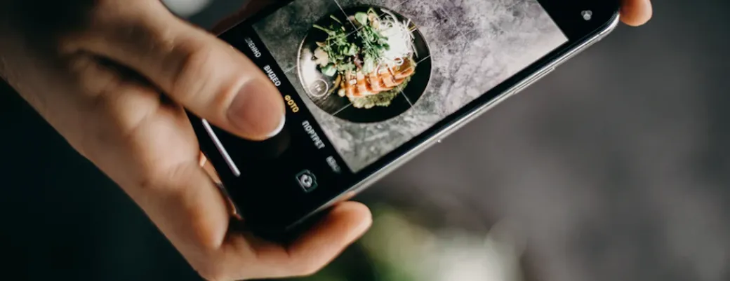 A hand photographing a plated dish with a phone