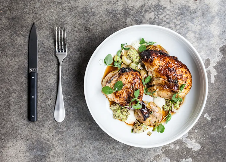 A plated roast chicken dish with peas and herbs, seen from above